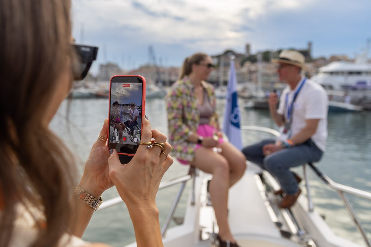 Guest filming an interview on the deck of a yacht with the Cannes waterfront behind