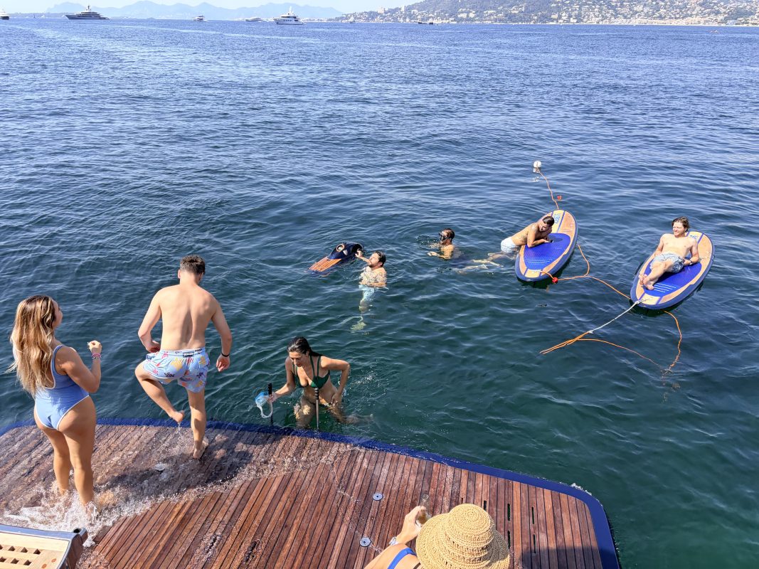 Guests swimming and relaxing on paddleboards behind a yacht at anchor in the Mediterranean