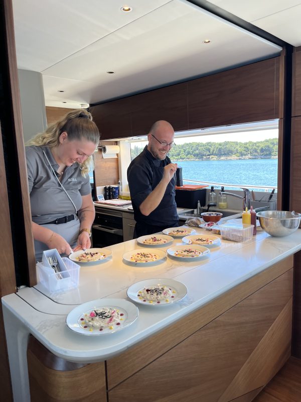 Two crew members preparing plated dishes on the counter of a yacht galley