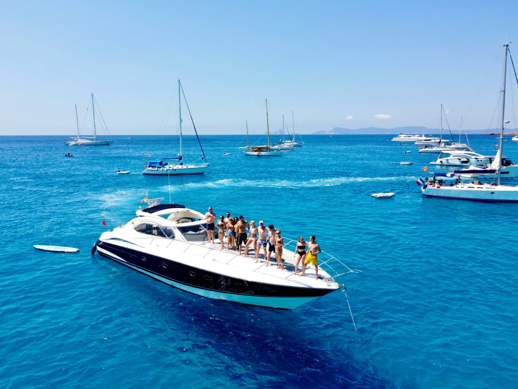 Guests standing on the bow of a motor yacht at anchor in clear blue water